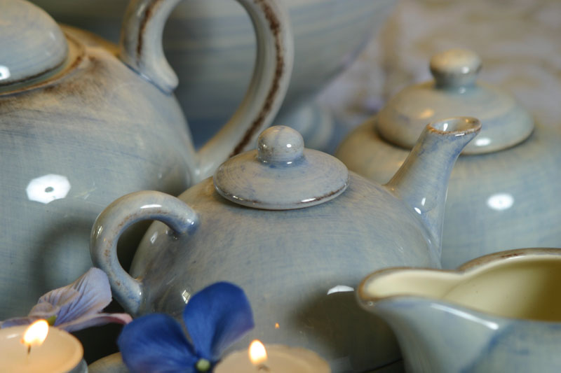 Light blue ceramic teapots and a creamer arranged with lit tea candles and blue flowers
