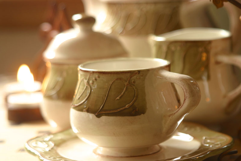 Cream-colored ceramic tea set with embossed green leaf designs, featuring a cup, saucer, sugar bowl, and creamer