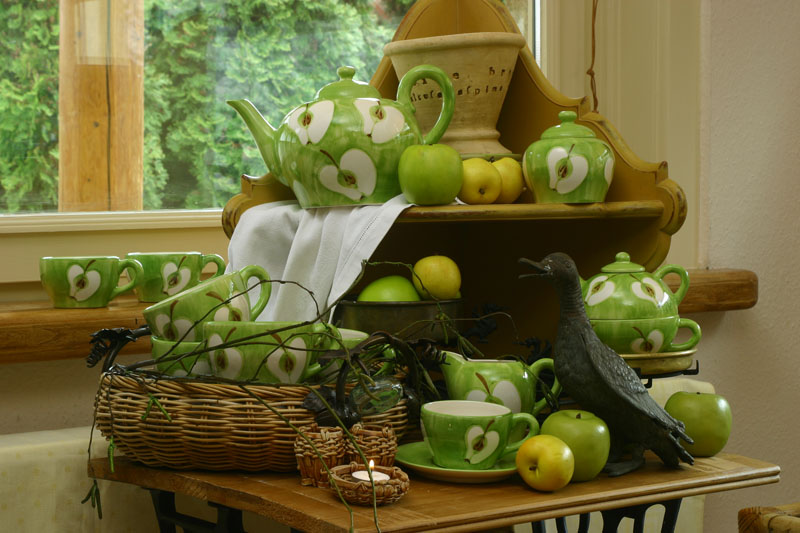 Green tea set with white apple patterns, real apples, and a bird figurine on a wooden table and shelf