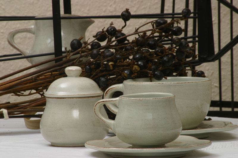 Off-white ceramic tea set with a cup, saucer, and lidded sugar bowl arranged with dried dark berries