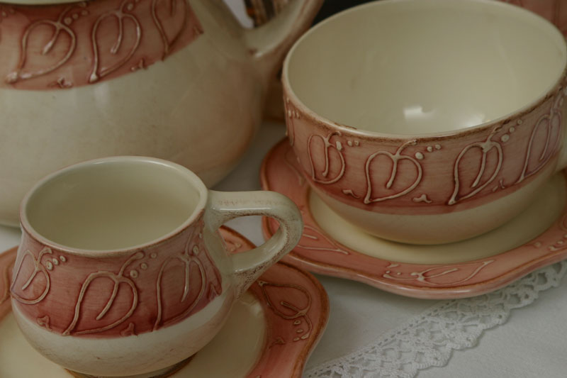 Cream-colored ceramic cups and saucers with a pink band featuring embossed leaf patterns