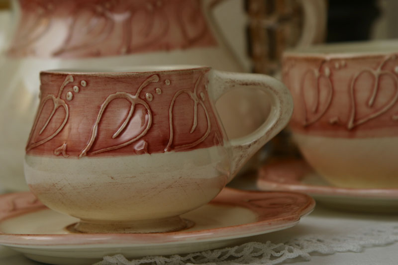 Cream ceramic teacup and saucer with embossed leaf patterns in a reddish-pink band