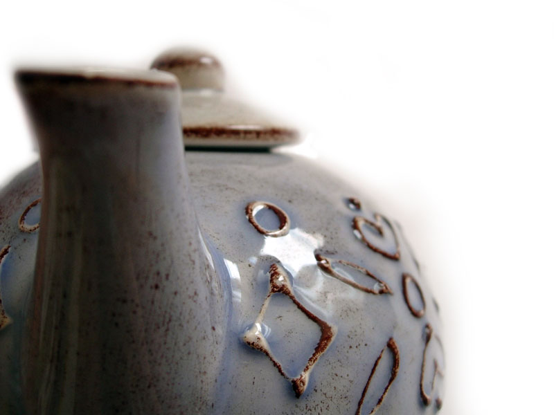 Close-up of a light blue ceramic teapot with brown speckles and embossed geometric patterns
