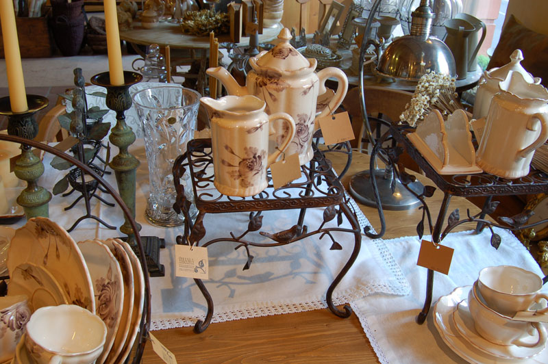 Tableware display with floral ceramic tea sets, wrought iron stands, and candlesticks