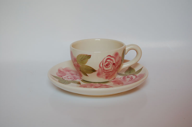 Cream-colored teacup and saucer with hand-painted pink roses and green leaves